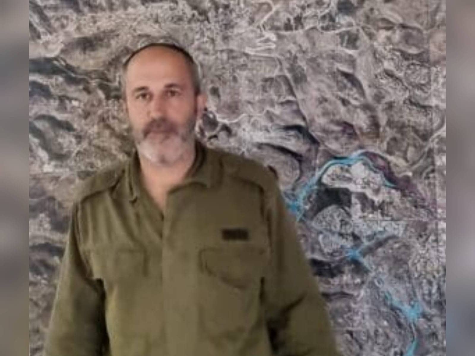 אריה קינג מביט למצלמה, מצולם במדי שטח על רקע מפת ירושלים