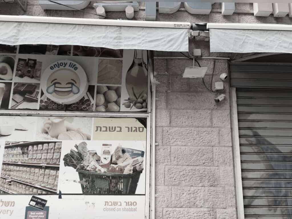 שלט “סגור בשבת” על סופר ירושלמי, לצד לוגו "enjoy life" עם אימוג’י בוכה מצחוק