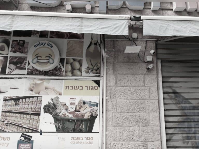 שלט “סגור בשבת” על סופר ירושלמי, לצד לוגו "enjoy life" עם אימוג’י בוכה מצחוק