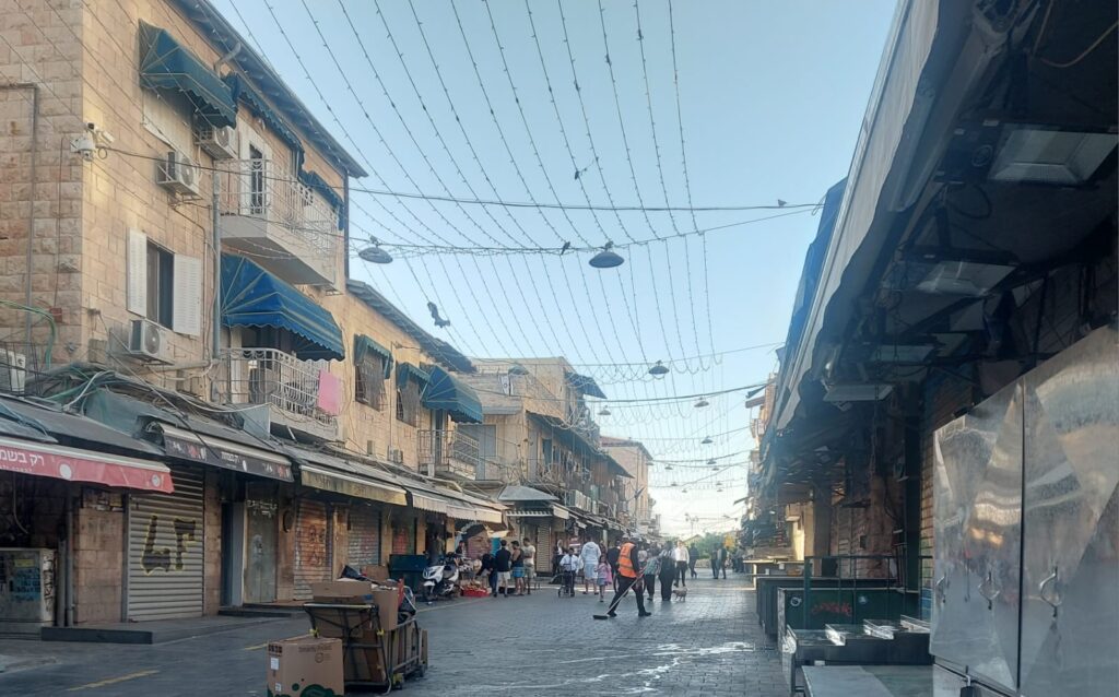 שוק מחנה יהודה בירושלים ביום בהיר, ממחיש את חיי היומיום בעיר לקראת מזג האוויר הצפוי
