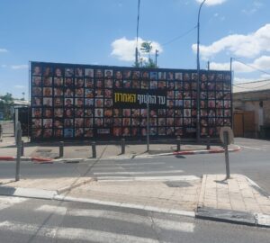 לוח ציבורי גדול בירושלים בסמוך למתחם הרכבת עם תצלומי החטופים והכיתוב "עד החטוף האחרון".