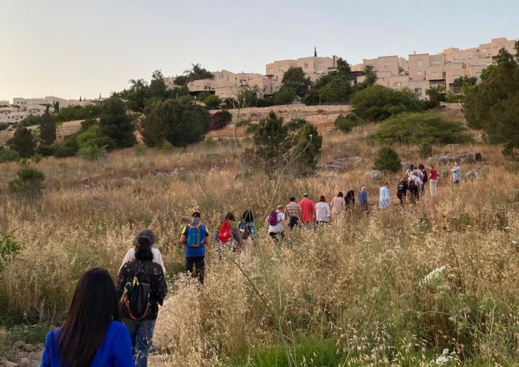 קבוצת אנשים בהליכה בנוף מודיעין, המחשה לקונספט חקר עירוני והשוואה לאופן שבו ירושלים מספרת את סיפורה דרך הליכה.