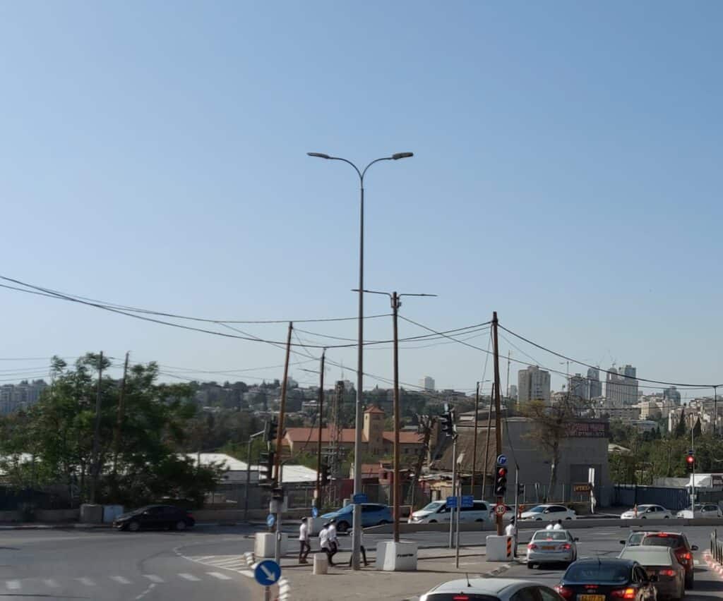 תמונת רחוב בירושלים עם תנועת מכוניות ואוטובוס, בניינים ברקע, ורמזור ירוק בבוקר בהיר