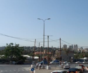 תמונת רחוב בירושלים עם תנועת מכוניות ואוטובוס, בניינים ברקע, ורמזור ירוק בבוקר בהיר