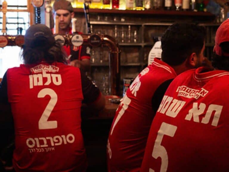 Fans of Hapoel Jerusalem sitting at a bar, wearing team jerseys