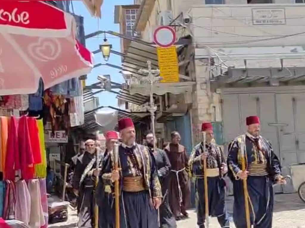 Christian monks in black robes march through Jaffa Gate in Jerusalem with wooden staffs, in a traditional religious procession