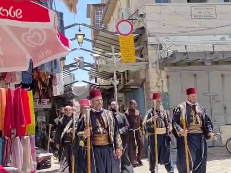 Christian monks in black robes march through Jaffa Gate in Jerusalem with wooden staffs, in a traditional religious procession