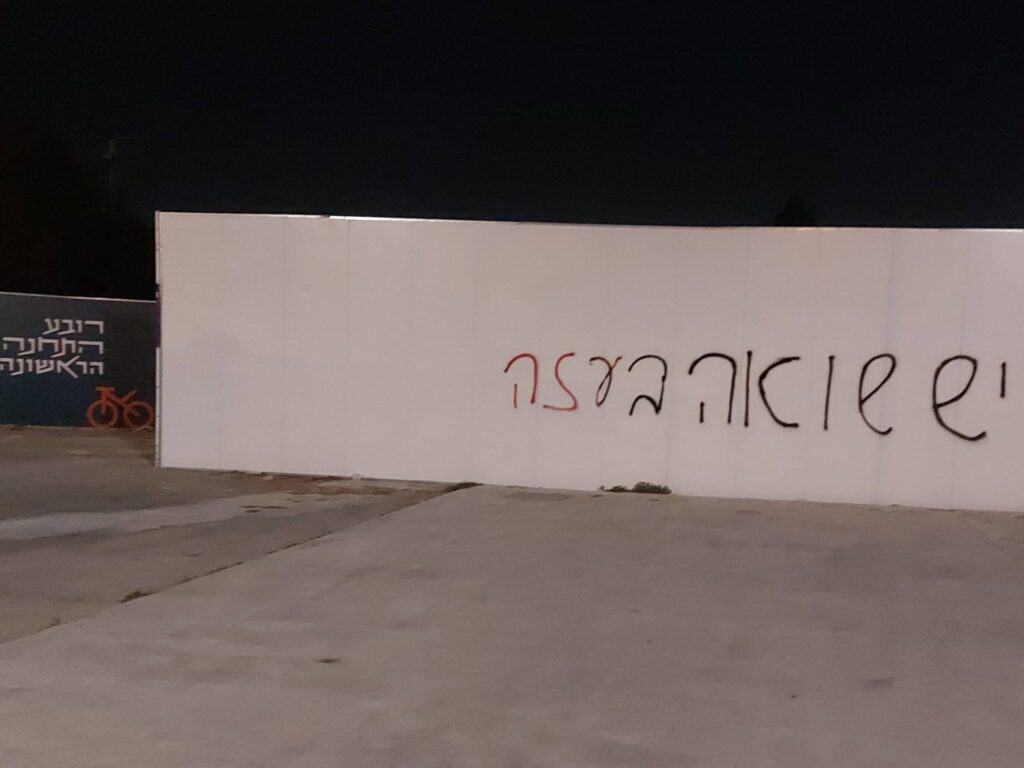 Graffiti in Jerusalem’s First Station complex reading “There is a Holocaust in Gaza,” spray-painted on a white wall at night