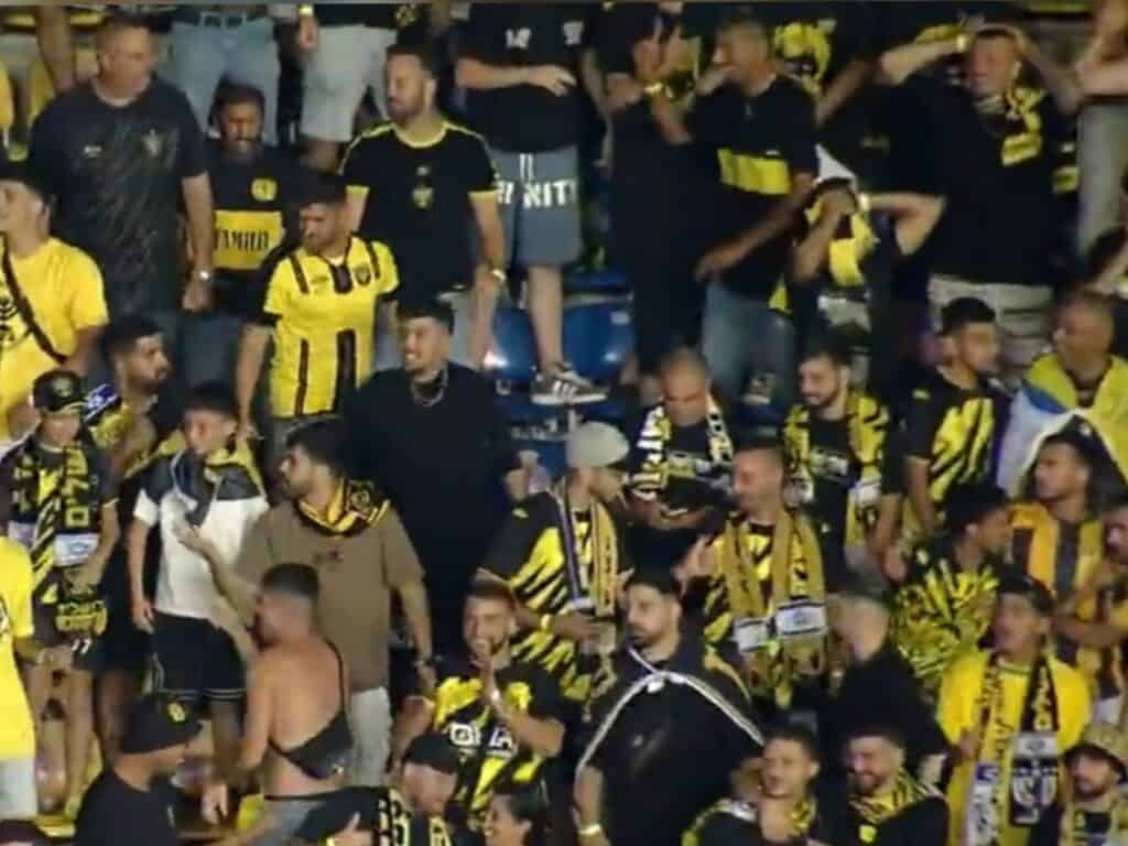 Beitar Jerusalem fans in yellow and black cheering passionately in the stands during the Conference League match in Bucharest