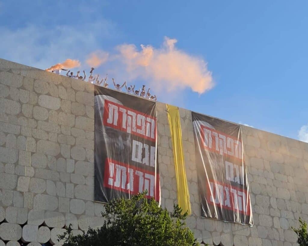 מפגינים על גג עם רימון עשן ושלטים בגבעת רם במחאת החטופים בירושלים